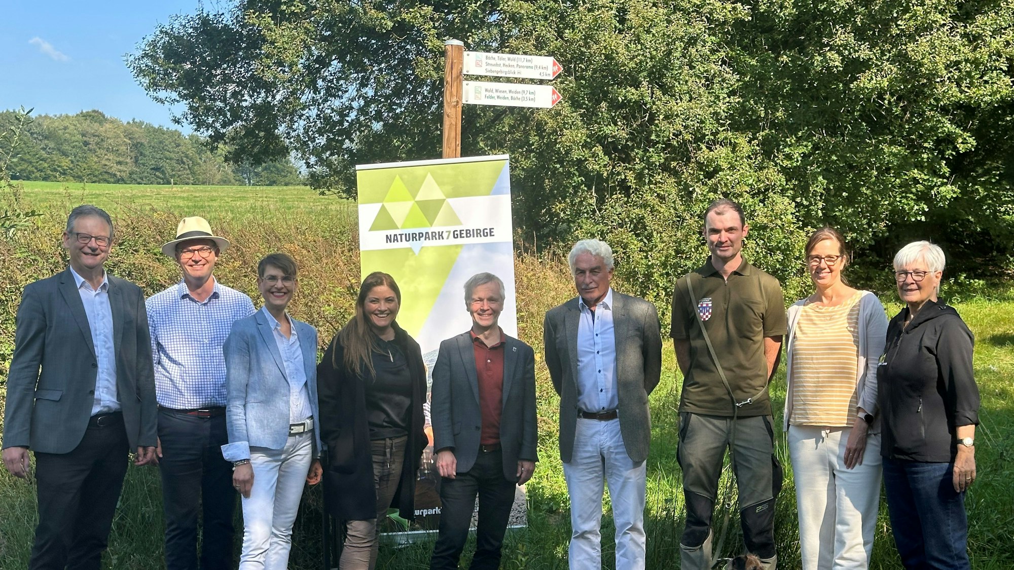 Fünf Männer und eine Frau vor einem Werbeschild