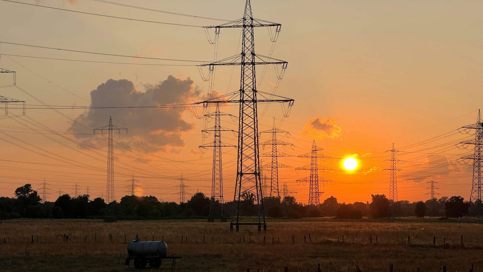 Das Bild zeigt einen Sonnenuntergang hinter Strommasten.