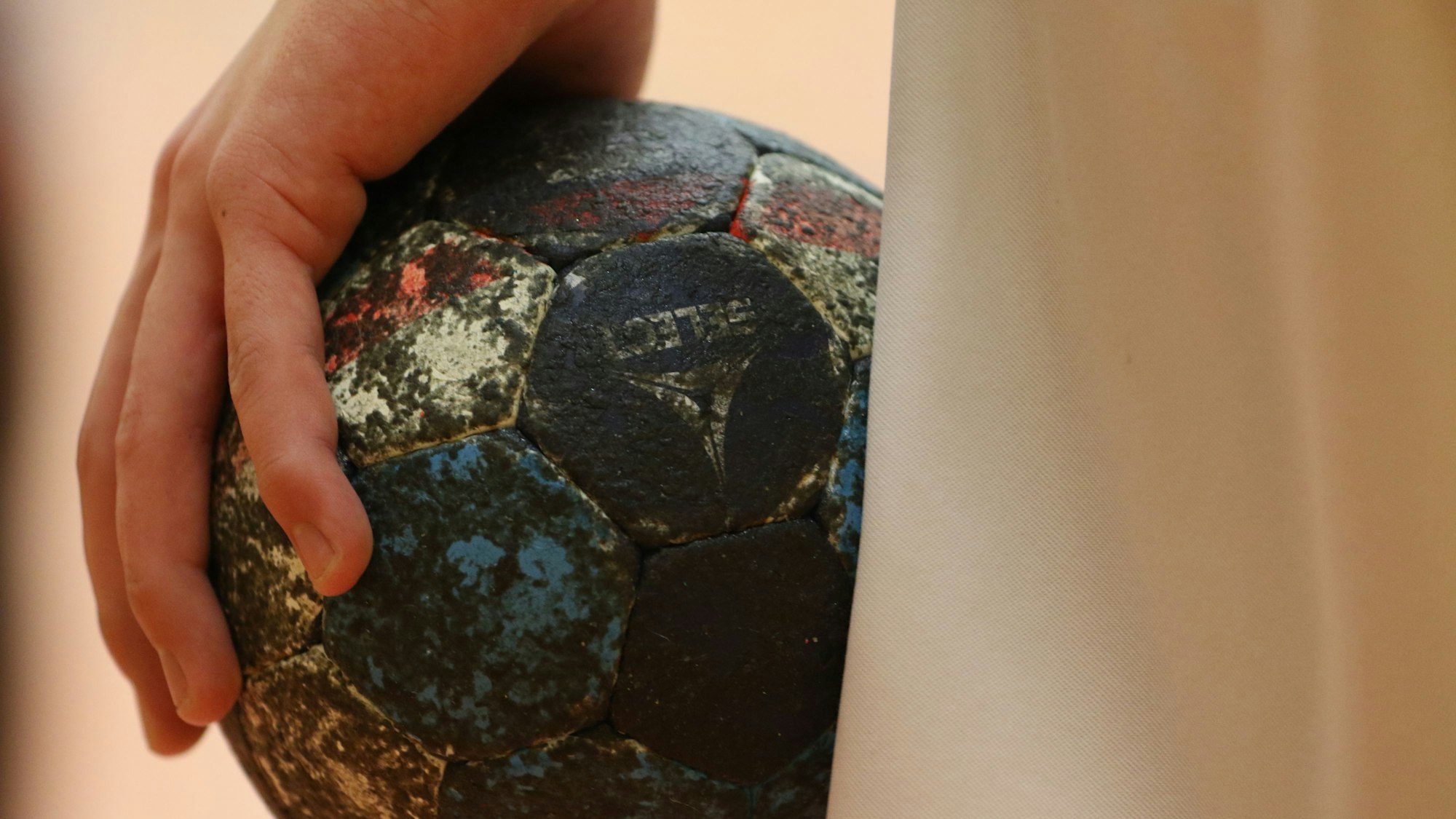 Ein beinahe schwarzer Handball liegt in einer Hand.