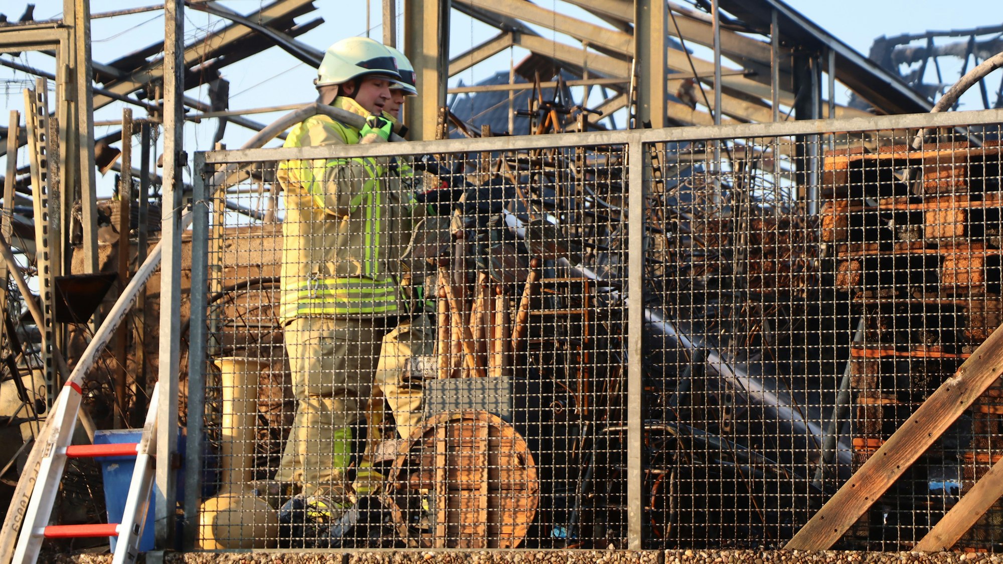 Ein Feuerwehr steht in einem Gewächshaus, das nur noch aus Gerippe besteht.