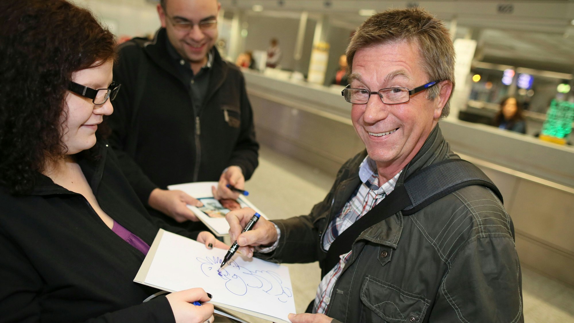 Der frühere Kaufhaus-Erpresser „Dagobert“ und heutige Karikaturist Arno Funke zeichnet am 06.01.2013 im Terminal 2 des Flughafens von Frankfurt am Main einem Fan eine Karikatur auf ein Blatt. Er wartet auf den Abflug nach Australien, wo er Teilnehmer des RTL-Dschungelcamps sein wird.