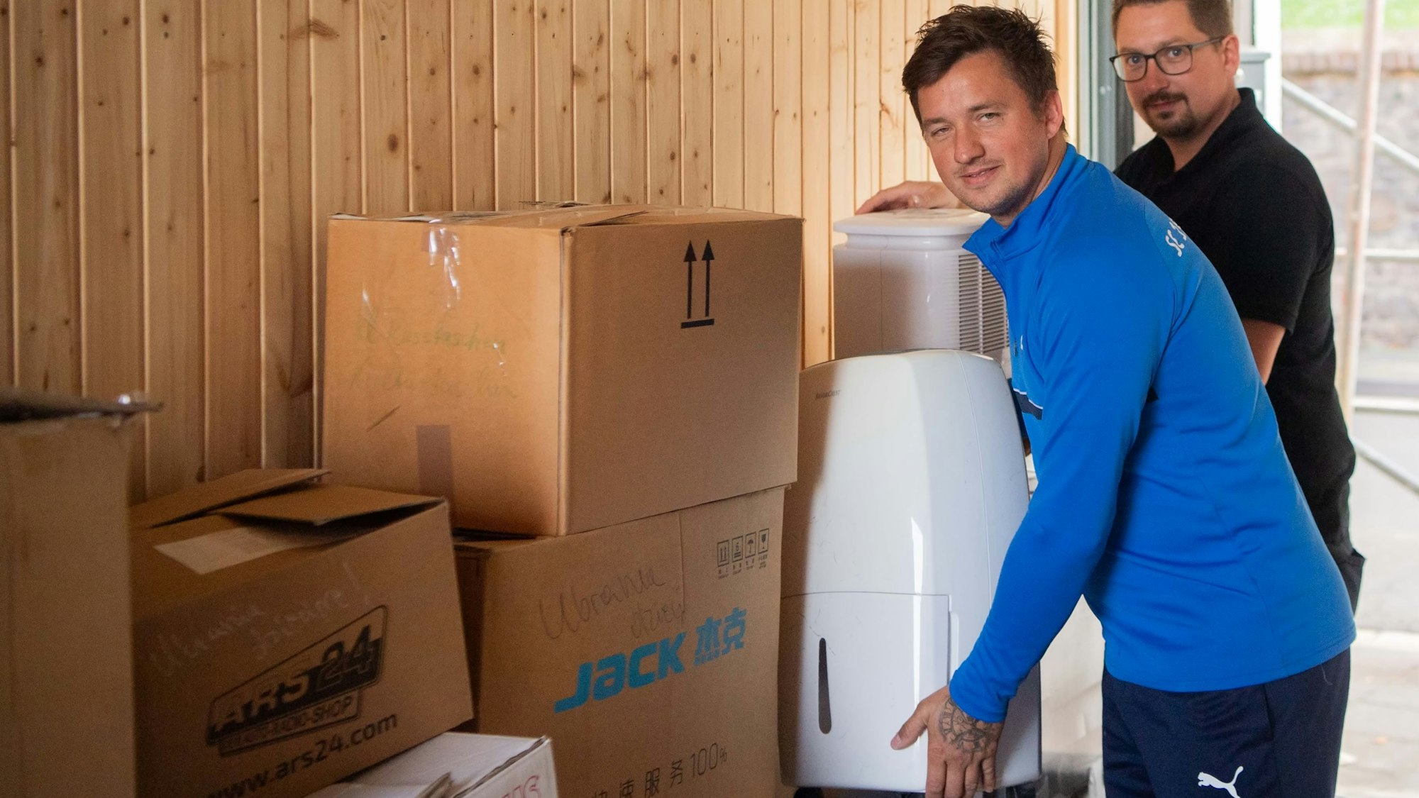 Das Bild zeigt zwei Männer, die jeweils ein Trocknungsgerät auf den Stapel mit Hilfsgütern stellen.