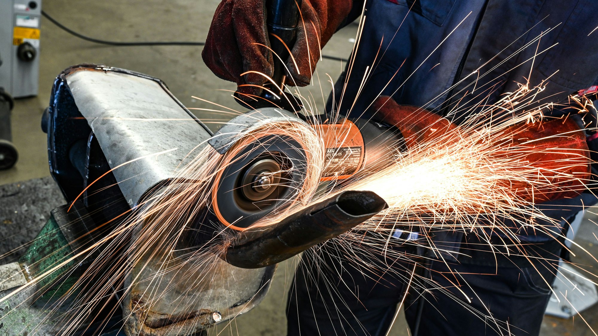 Ein Auszubildender im KFZ-Handwerk schneidet mit einer Flex einen alten Auspuff auf. In der Branche gibt es über 16.000 offene Stellen.