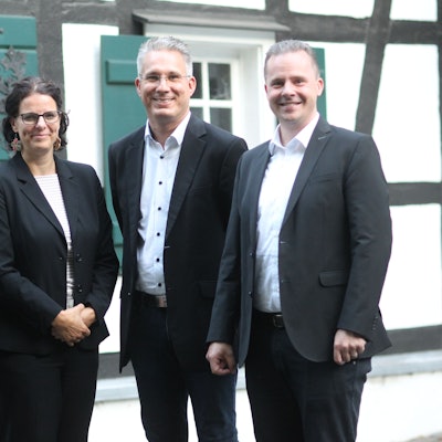 Eine Frau in einem dunklen Kostüm und drei Männer in grauen Anzügen