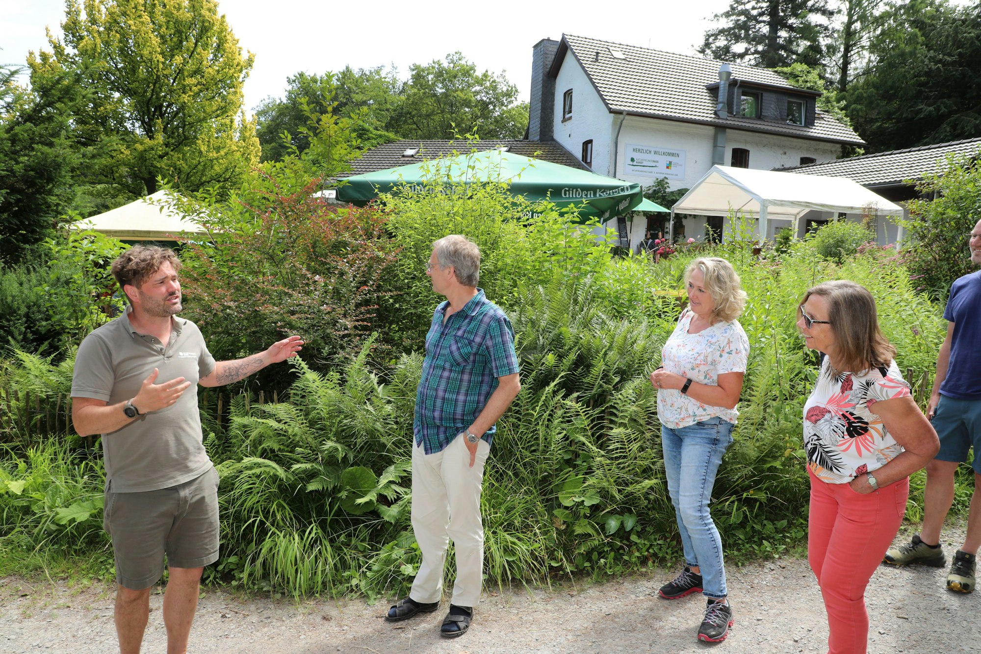Erlebnispädagoge und Pächter des Naturfreundehauses Hardt, Benjamin Stapf, steht mit Gästen vor dem Naturfreundehaus Hardt in Bergisch Gladbach.