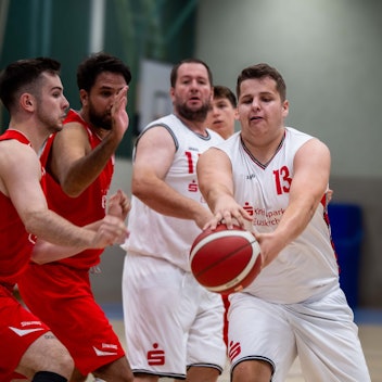 Ein Basketballspieler aus Zülpich greift während eines Testspiels nach dem Ball. Mitspieler und Gegenspieler schauen zu.