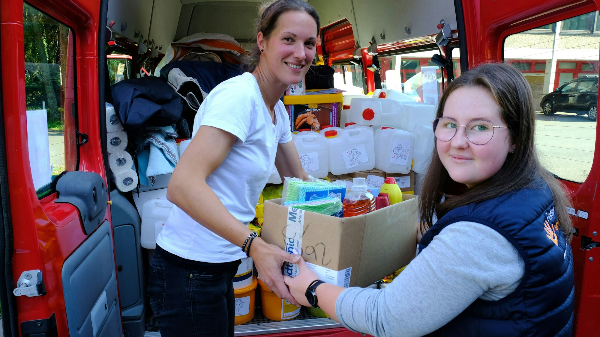 Das Bild zeigt Rebecca Müller und Laura Meyer, wie sie eine Kiste mit Hilfsgütern in einen Transporter laden.