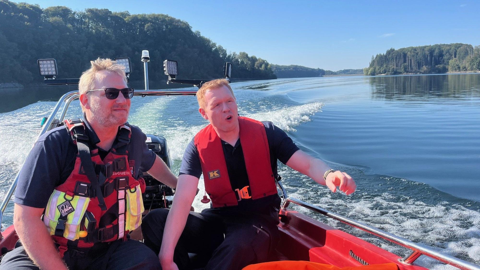 Zwei Feuerwehrleute fahren mit einem Boot über das Wasser.