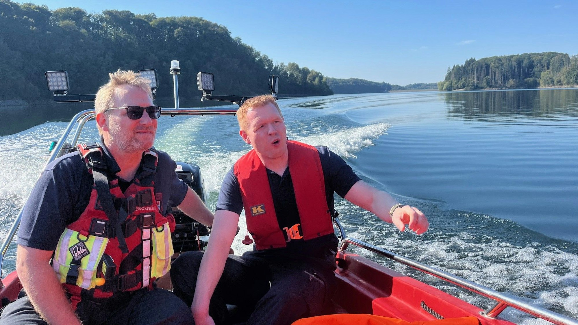 Zwei Feuerwehrleute fahren mit einem Boot über das Wasser.