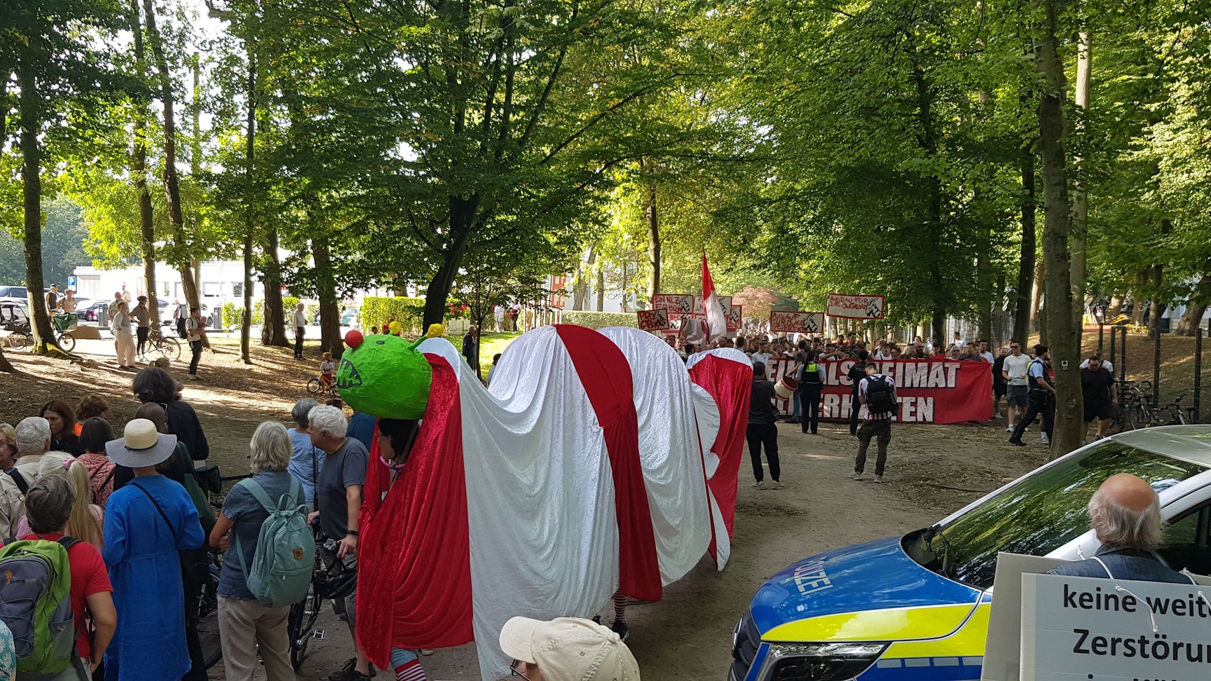 Protest der Bürgerinitiative Grüngürtel für Alle am Geißbockheim gegen den Bau des Jugendleistungszentrums.
Im Hintergrund stören etwa 150 Ultras durch Gesänge den Spaziergang der Ausbaugegner.