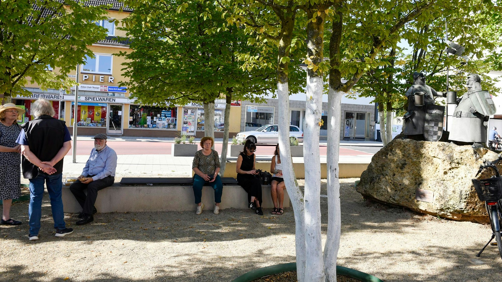 Menschen sitzen auf dem Viry-Châtillon Platz im Schatten der Bäume.