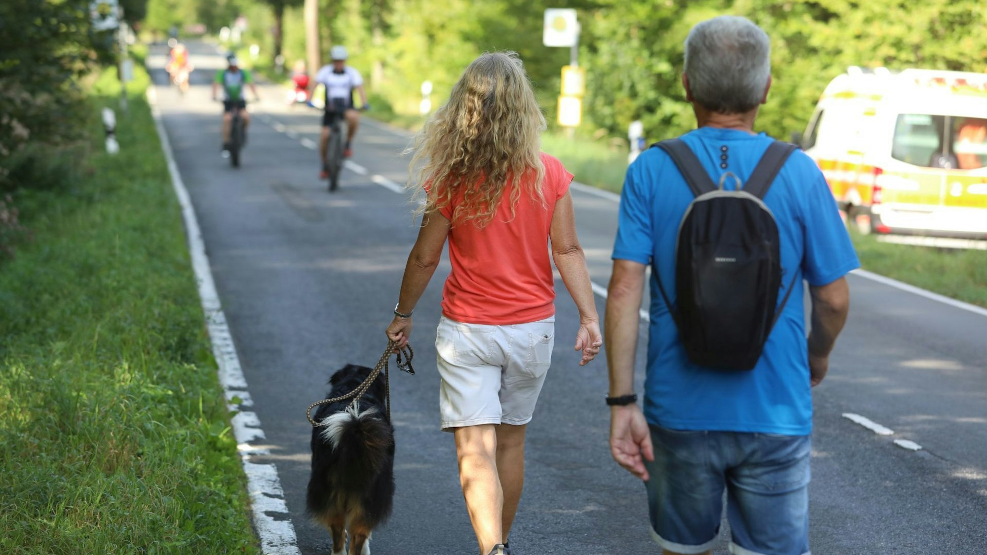 Eine Frau und ein Mann gehen die Straße entlang und halten einen Hund an der Leine.