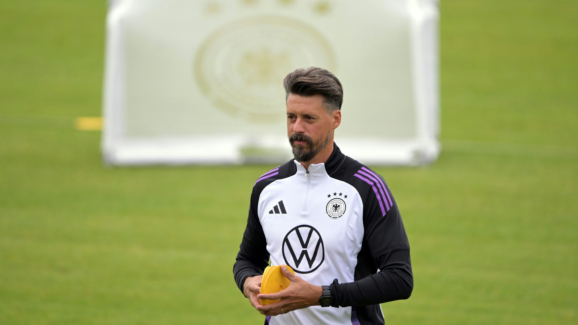 Deutschlands Co-Trainer Sandro Wagner während eines öffentlichen Trainings auf dem Fußballplatz. Er trägt Trainingskleidung, im Hintergrund ist ein Tor zu sehen.