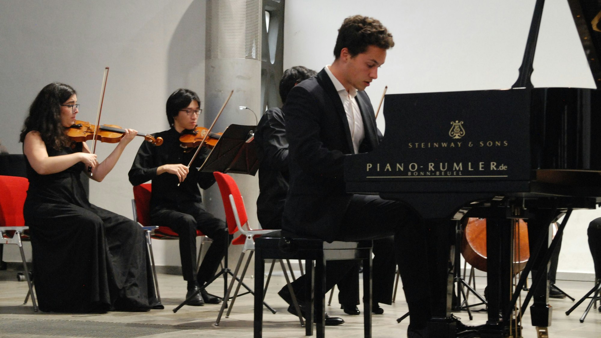 Nikola Meeuwsen am Klavier, im Hintergrund sind zwei Streicher des Folkwang Orchesters zu sehen.