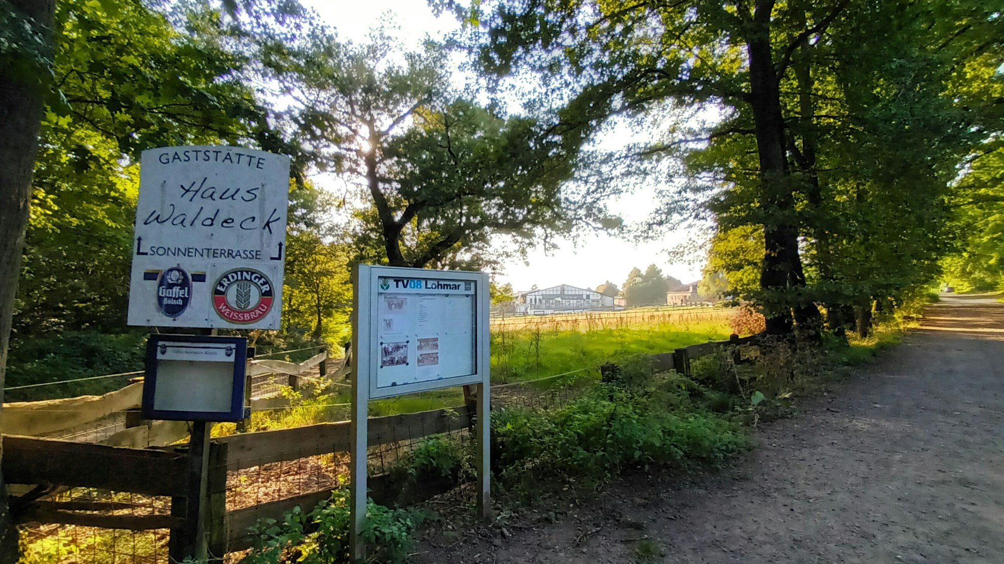 Eine umzäunte Wiese an einem Waldweg mit einem Hinweisschild
