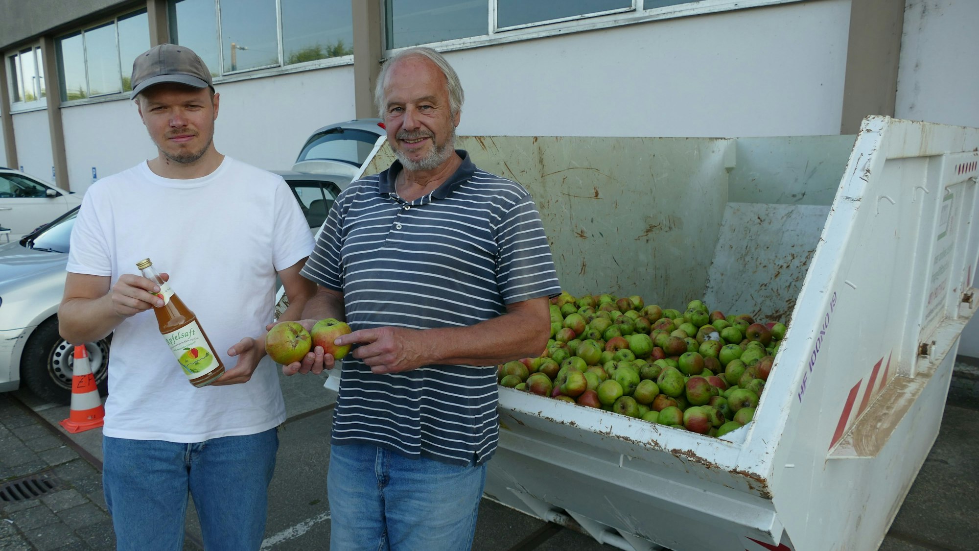 Zwei Männer stehen vor einem Container, der mit Äpfel gefüllt ist.