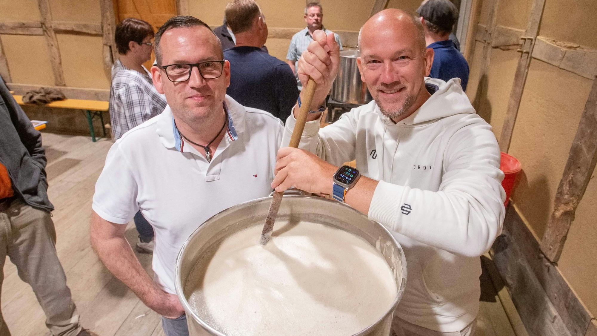 Das Foto zeigt zwei Männer, die in einem großen Topf mit Maische rühren.