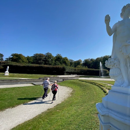 Zu sehen sind zwei Spaziergänger vor der Großen Fontäne im Schlosspark.