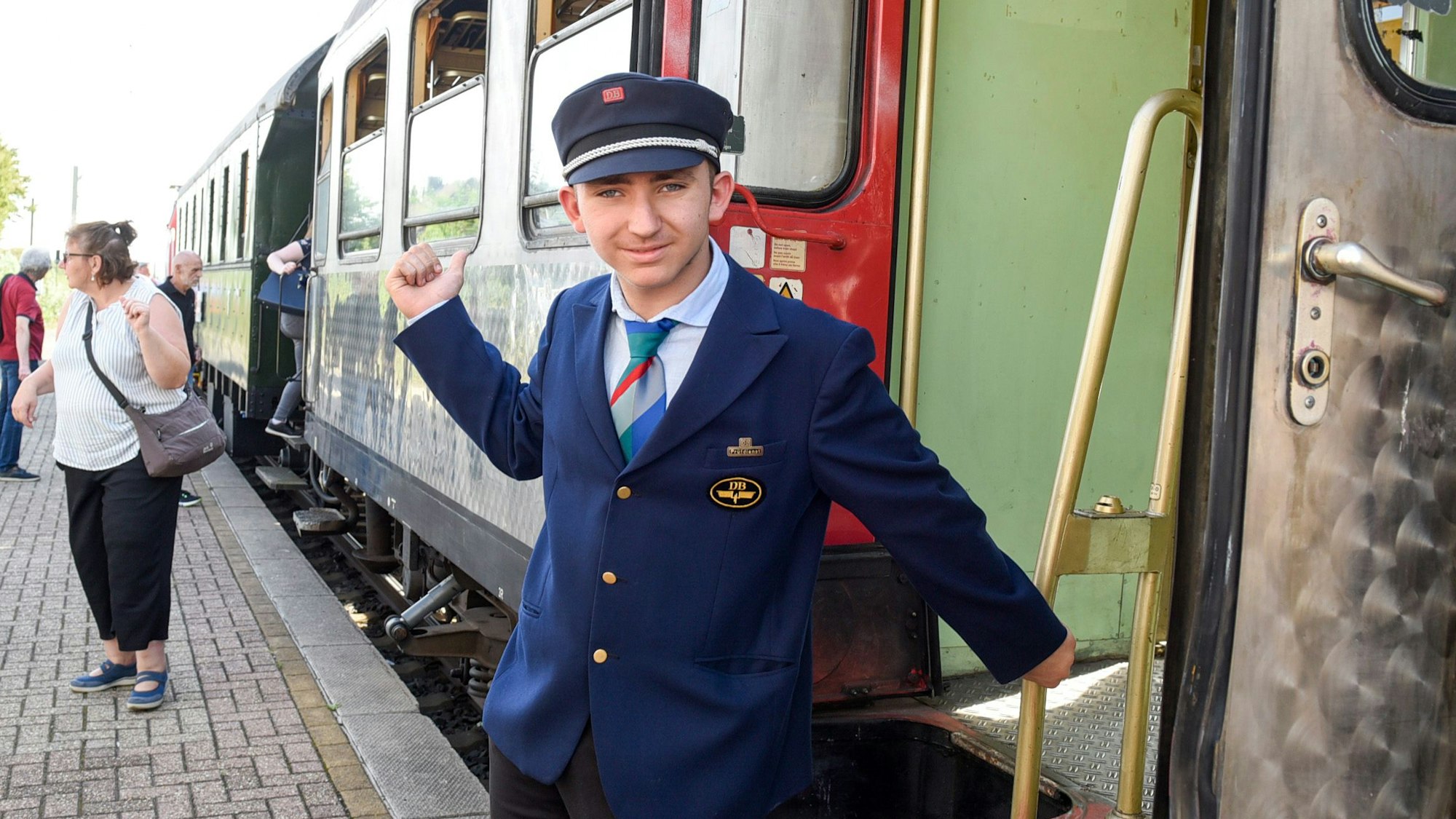 Ein Mann steht in der Originaluniform eines DB-Prüfers aus den 1960er Jahren vor einem Zug.