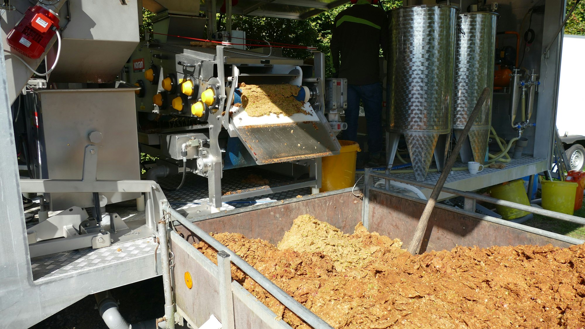 Ein Anhänger mit braunem Inhalt steht vor einer Maschine.