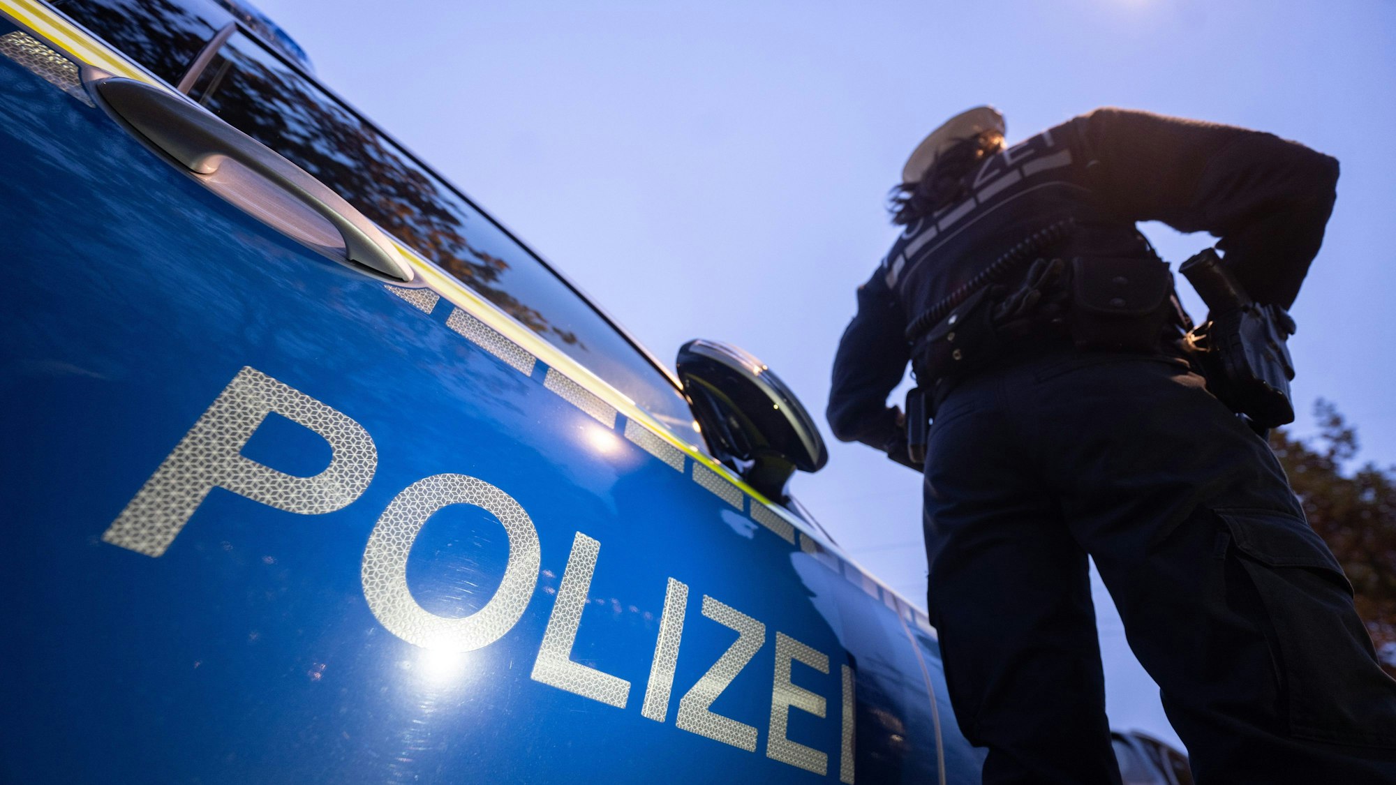 Das Bild ist ein Symbolfoto und zeigt eine Polizeibeamtin an einem Streifenwagen.