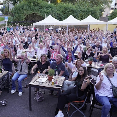 Das Foto zeigt vollbesetzte Reihen des Publikums bei einer Veranstaltung im Kulturbiergarten unter freiem Himmel.