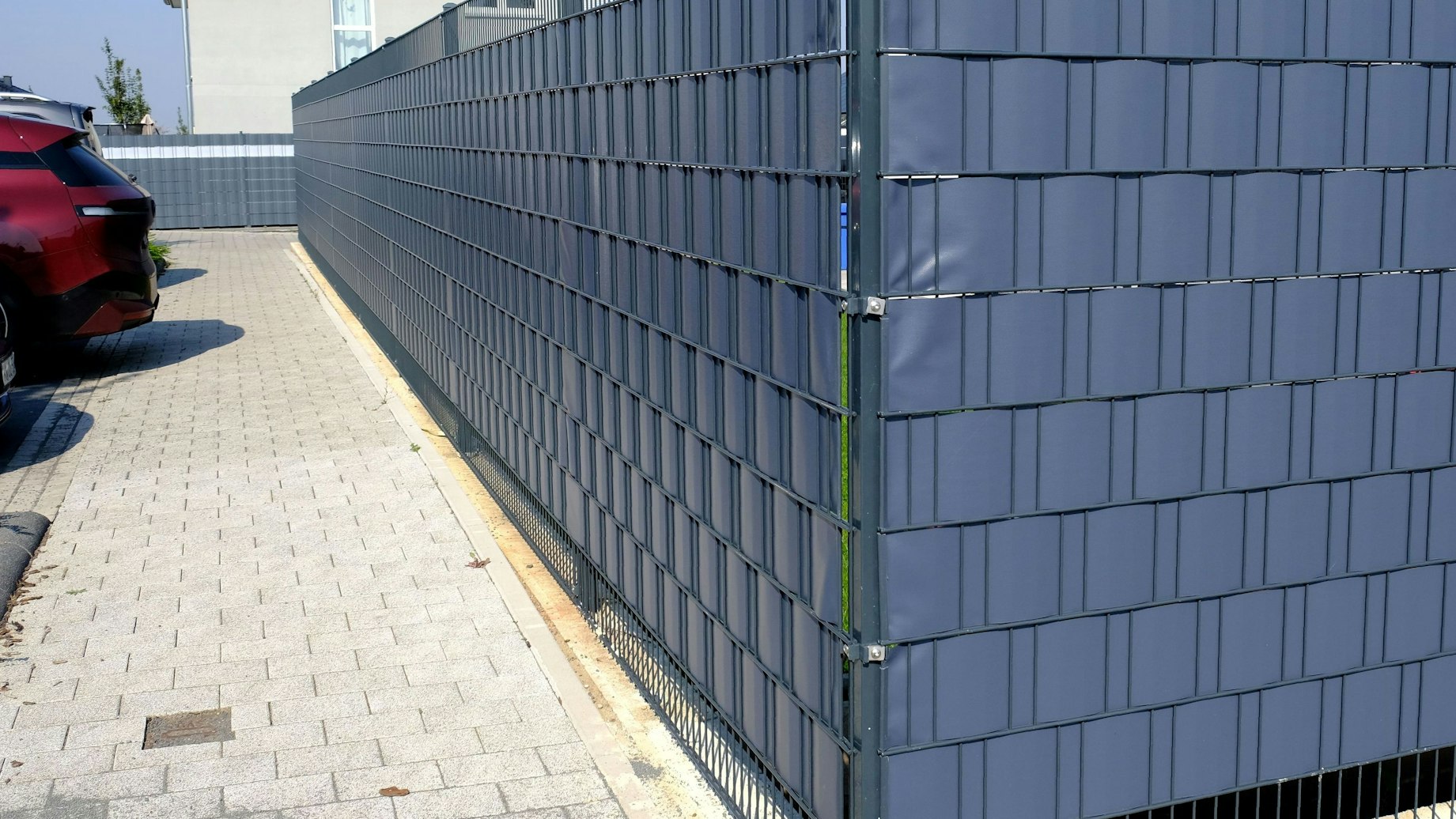 Das Foto zeigt eine Grundstückseinfriedung aus einem Stabgitterzaun mit Plastikeinflechtungen.