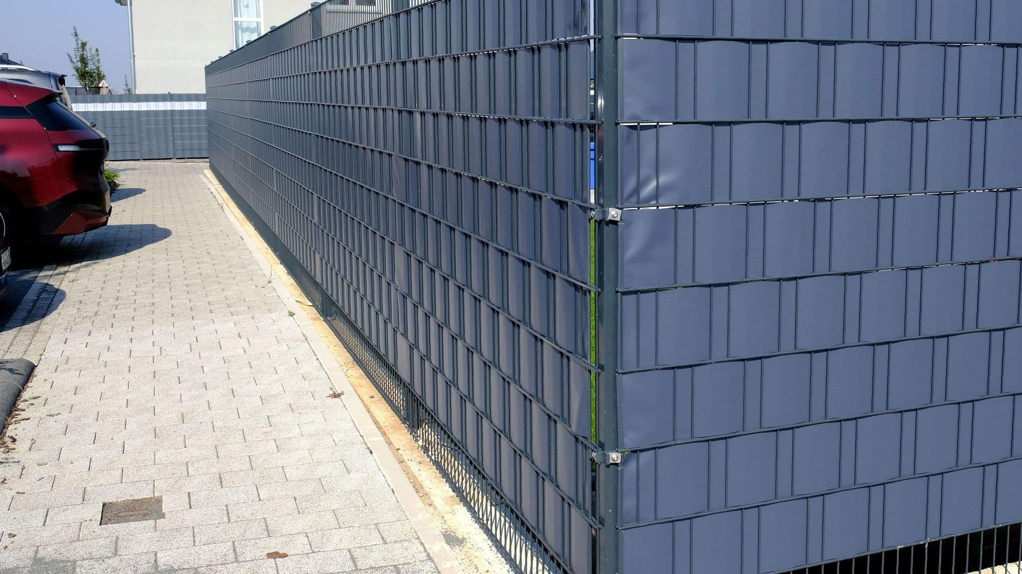 Das Foto zeigt eine Grundstückseinfriedung aus einem Stabgitterzaun mit Plastikeinflechtungen.