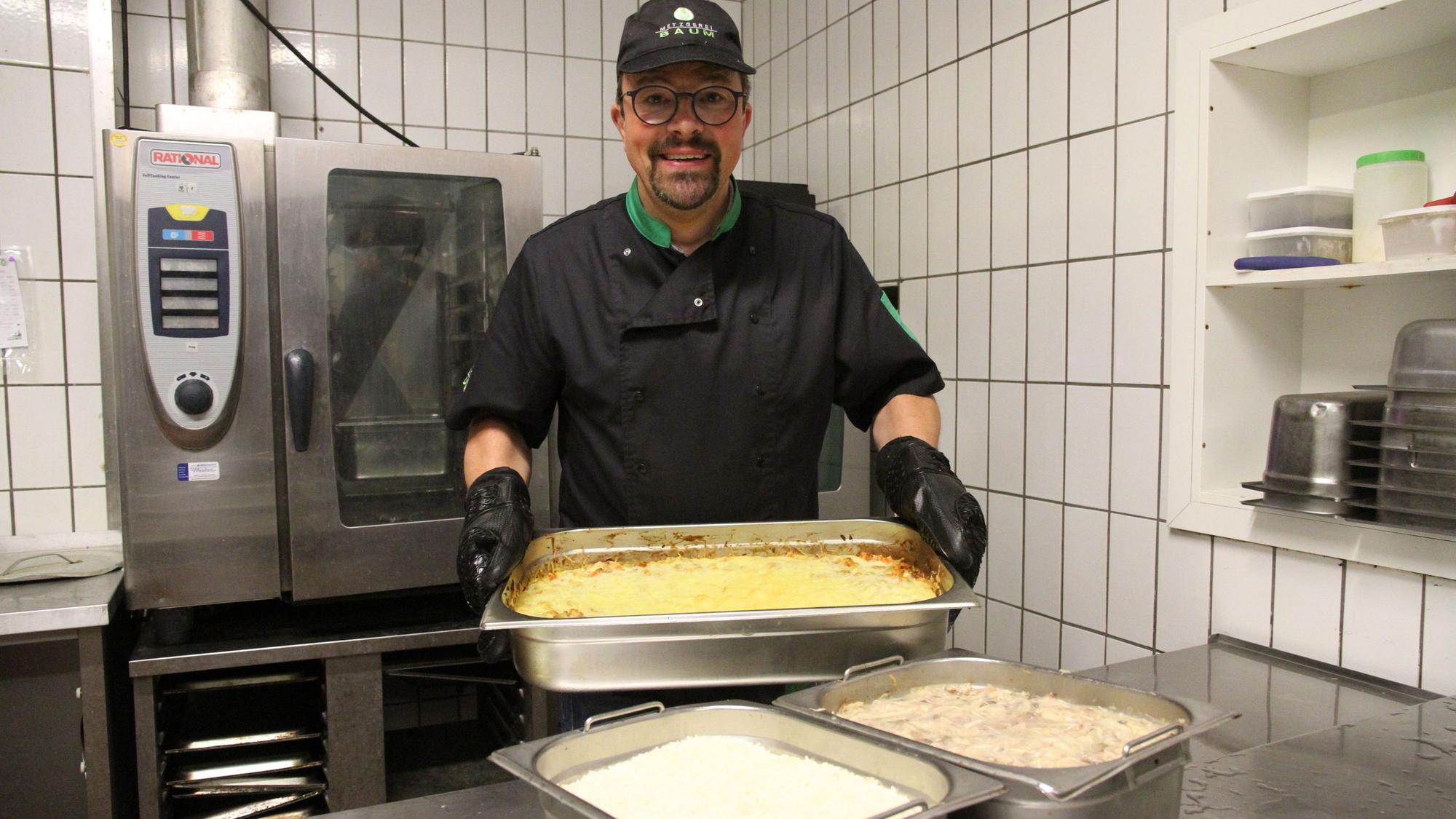 Ein Mann hält in einer Profiküche eine Auflaufform in den Händen.