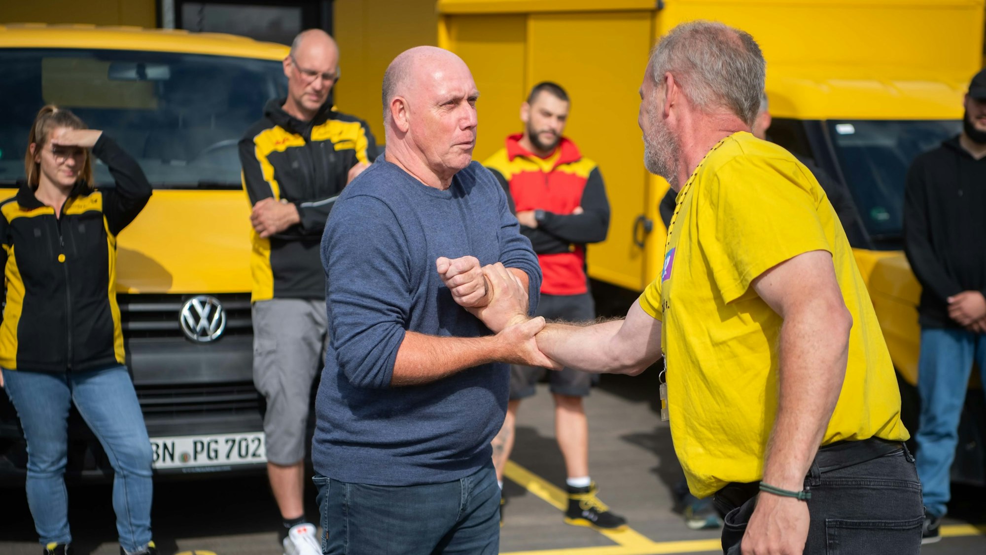 Michael Pfaff hat einen der Lehrgangsteilnehmer am Arm gepackt, in Hintergrund schauen weitere Zusteller zu.