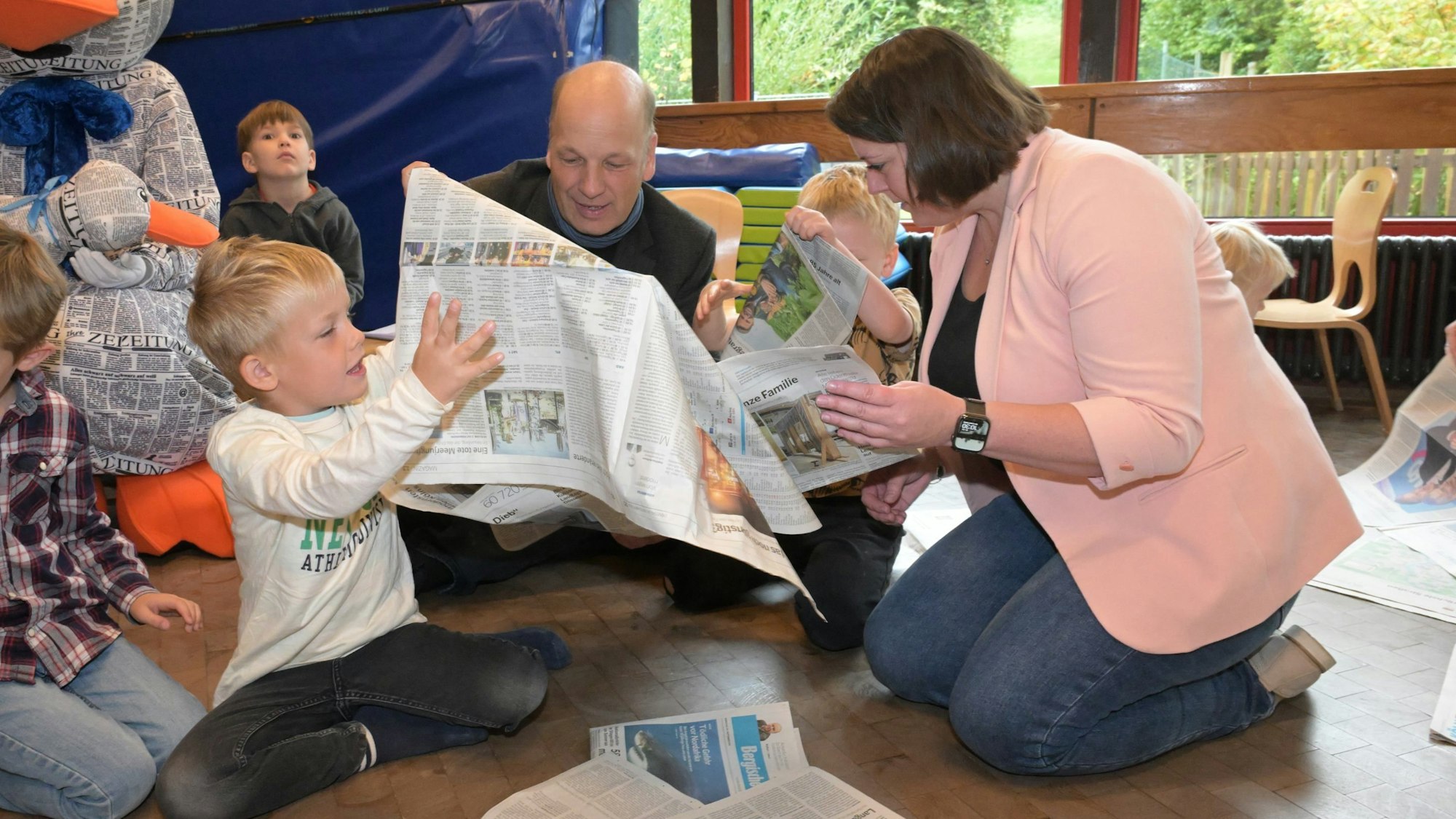 Heike Trompetter von der Kreissparkasse Köln und BLZ-Redaktionsleiter Guido Wagner stöbern mit den Kindern der KEO Kita Eichenweg Overath in der Bergischen Landeszeitung.