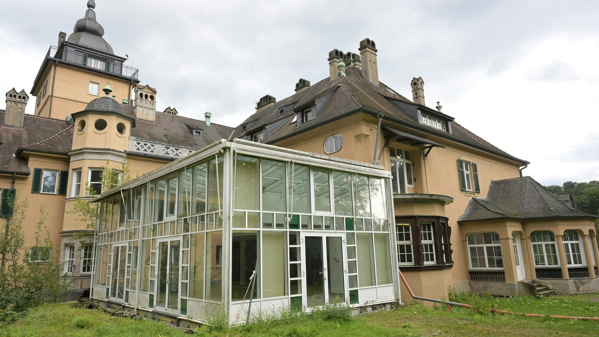 Eine etwas höhere Wiese ist vor der Rückseite von Schlosshotel Lerbach und einem älteren Erweiterungsbau zu sehen.