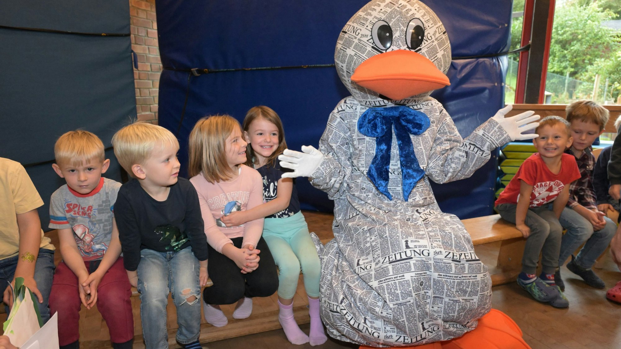 Paula Print sitzt in der KEO Kita Overath Eichenweg auf einer Bank zwischen Kindern.