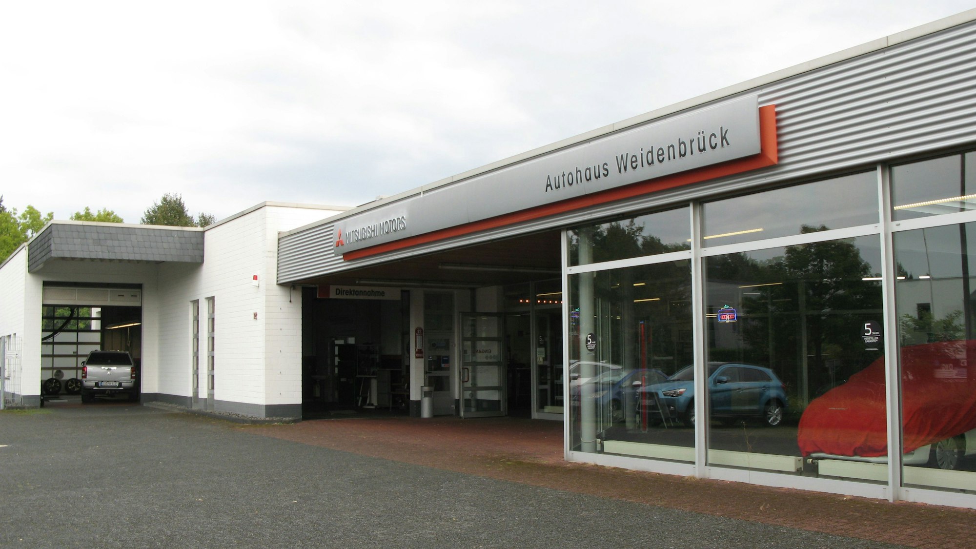 Ein Autohaus mit großen Schaufenstern und Einfahrt in eine Werkstatt.