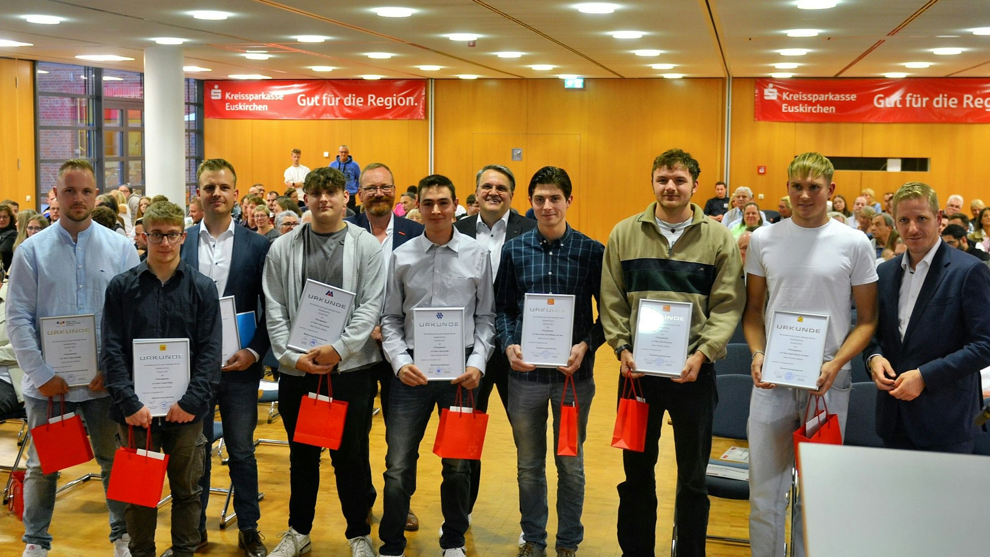 Das Bild zeigt die Prüfungsbesten, die ihre Urkunden in Händen halten, mit Landrat Markus Ramers.