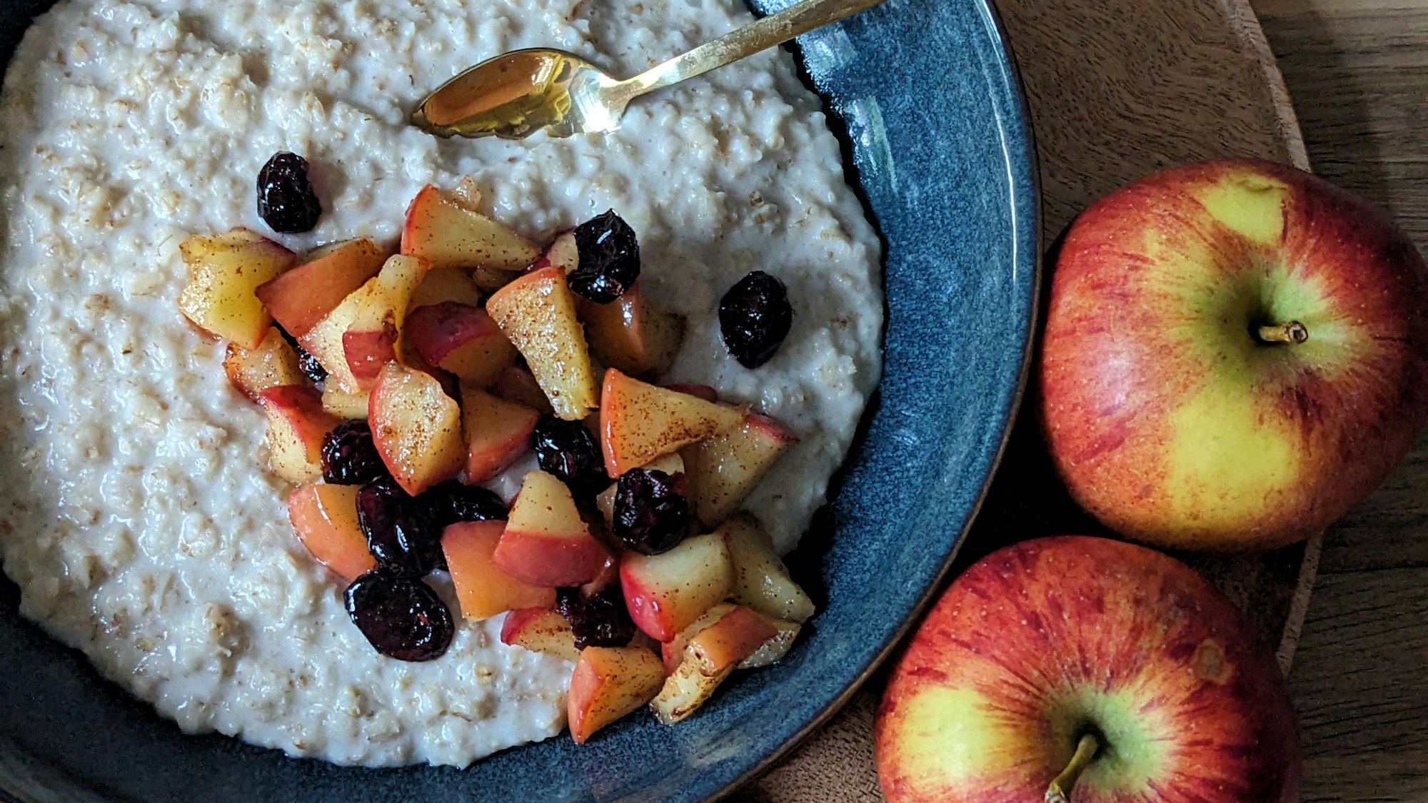 Bratäpfel, Cranberrys, Zimt liegen in einer Schüssel auf dem Porridge.