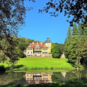 Schlosshotel Lerbach ist hinter dem Schlossteich zwischen Bäumen zu sehen.