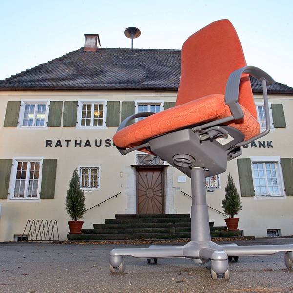 Ein Rathaus, davor ein Bürostuhl auf Rollen.