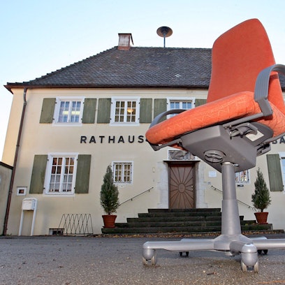 Ein Rathaus, davor ein Bürostuhl auf Rollen.