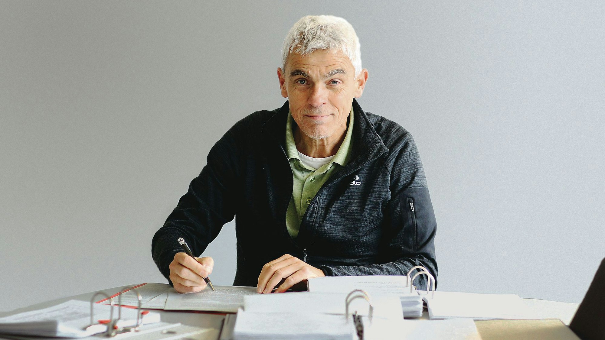 Ein grauhaariger Mann sitzt an vielen Akten.