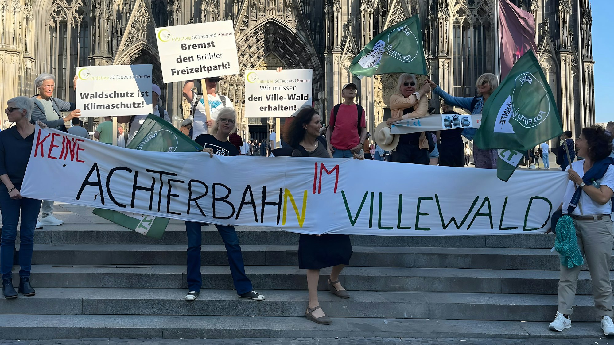 Zu sehen sind die Aktiven des Klimabündnisses, die ein großes Transparent mit der Aufschrift „Keine Achterbahn im Villewald“ halten.