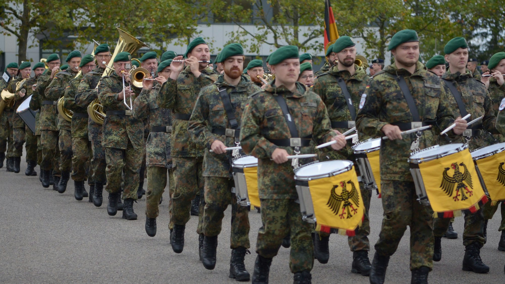 Die Orchestermusiker ziehen in Reih und Glied über den Kasernenhof, vorne Trommler, dahinter Flötisten und Musiker mit Blechblasinstrumenten.