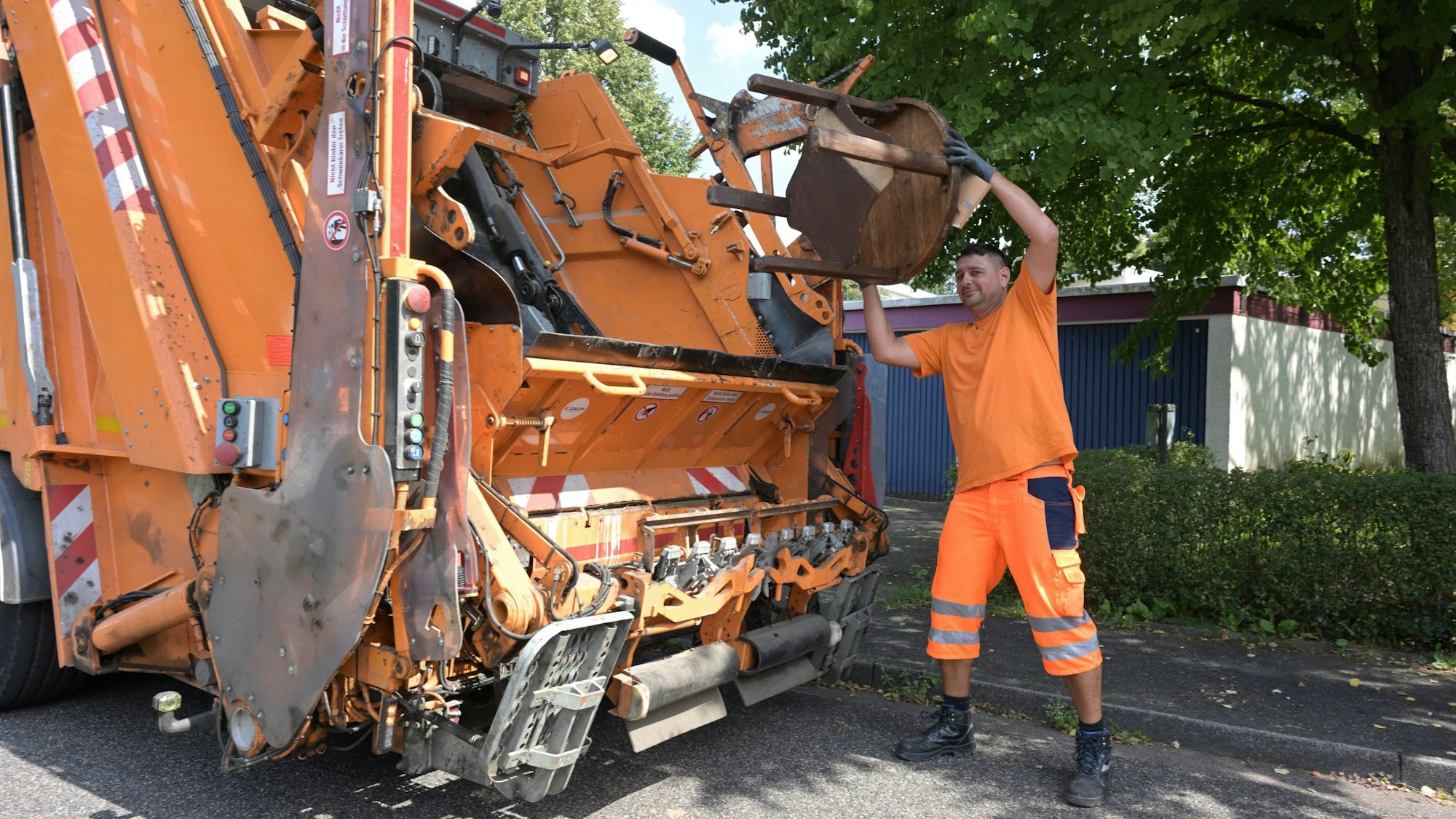 Ein Mitarbeiter der Müllabfuhr wirft einen Stuhl in ein Sperrmüll-Fahrzeug.