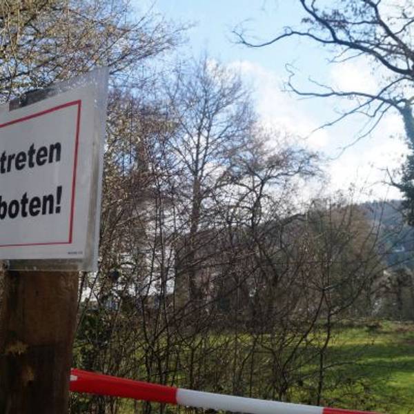 Ein „Betreten verboten!“-Schild hängt an einem Pfahl, dahinter ist rotweißes Flatterband zu sehen.
