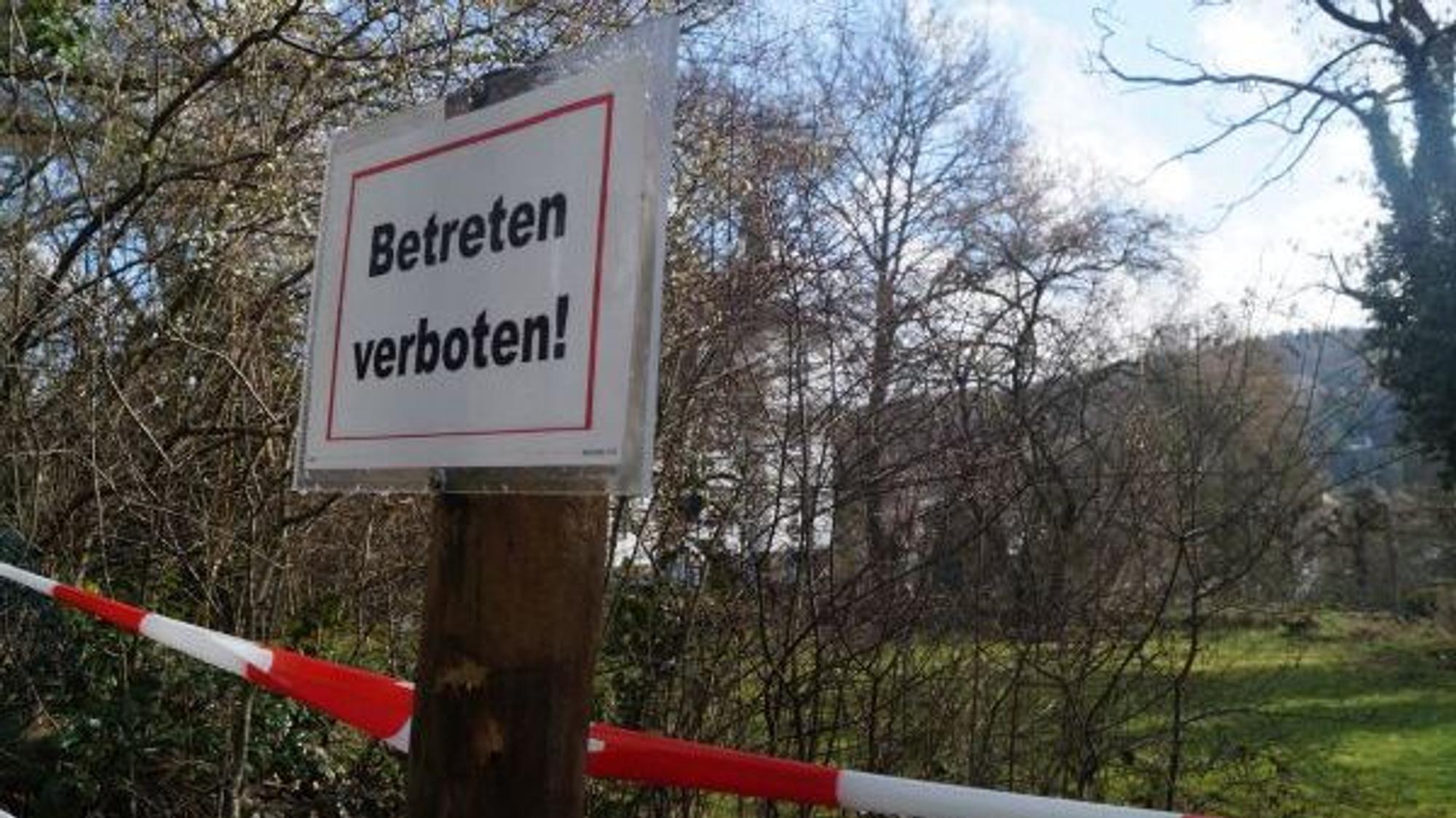 Ein „Betreten verboten!“-Schild hängt an einem Pfahl, dahinter ist rotweißes Flatterband zu sehen.