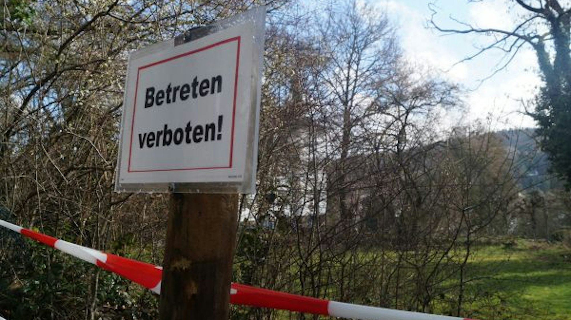 Ein „Betreten verboten!“-Schild hängt an einem Pfahl, dahinter ist rotweißes Flatterband zu sehen.