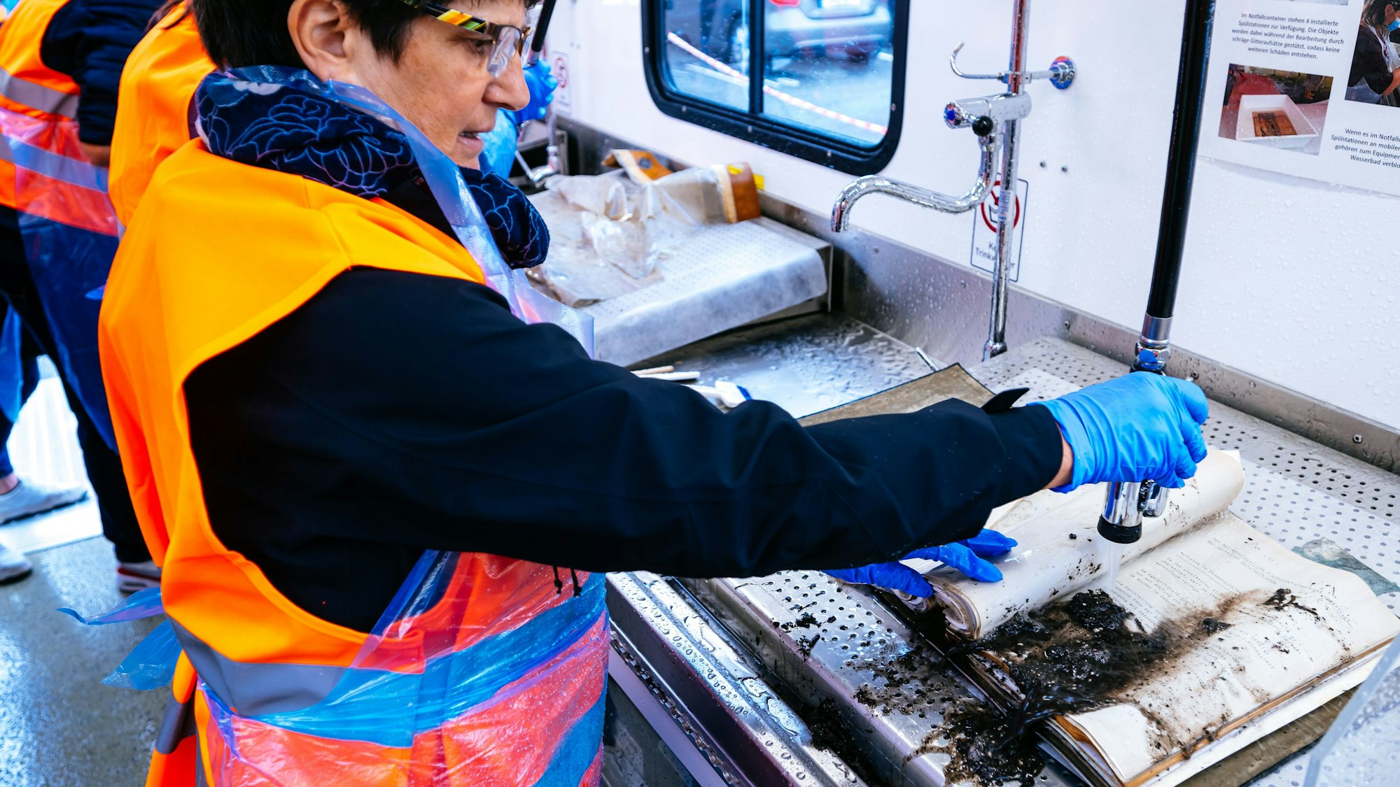 Bei einer Notfallübung spült eine Mitarbeiterin einer Bibliothek ein beschädigtes Buch mit einer Brause ab.
