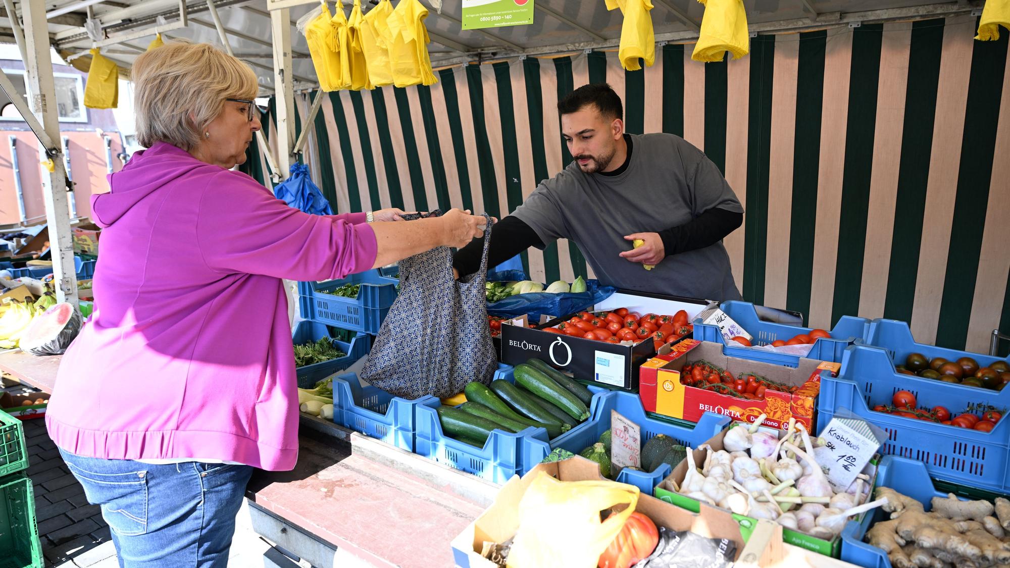Ein Händler bedient auf einem Wochenmarkt eine Kundin.