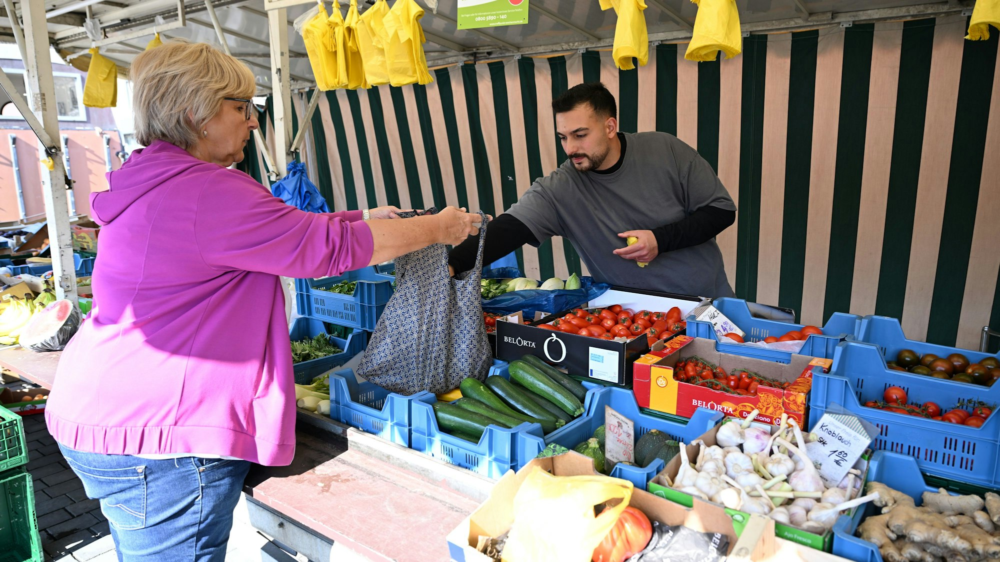 Ein Händler bedient auf einem Wochenmarkt eine Kundin.
