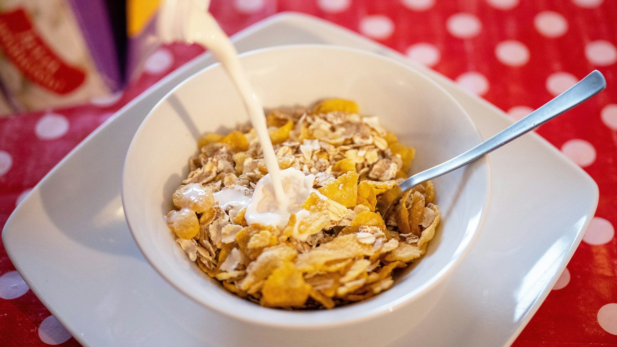 Das Bild zeigt eine Schale mit Müsli, in die Milch gegossen wird.